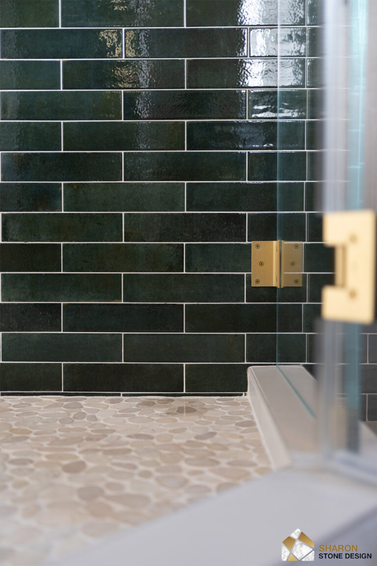 Palo Alto bathroom remodel hardware detail with a square brushed brass shower hinge clamped to frameless glass against the mottled green tile, above the cream pebble mosaic floor and marble-look shower curb.