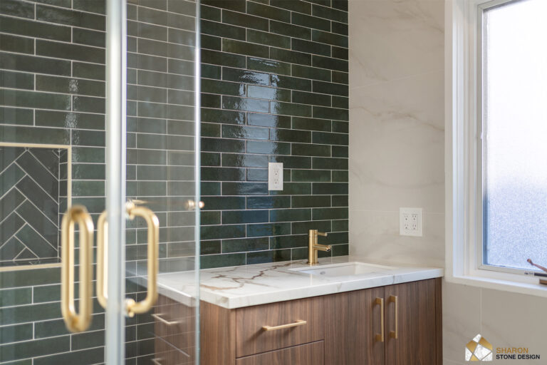 Palo Alto bathroom remodel looking past the brass shower door handles to the walnut vanity, its Calacatta-look top and brass faucet set against the green tile wall beside a frosted window.