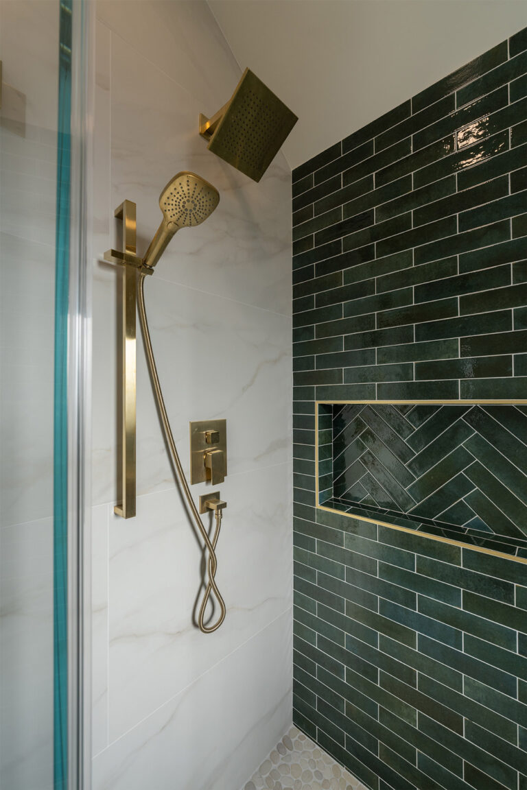 Palo Alto bathroom remodel shower fittings detail with a square brushed brass rain head, a handheld on a brass slide bar, and a square thermostatic valve set against white marble-look porcelain beside the green tiled shampoo niche wall.
