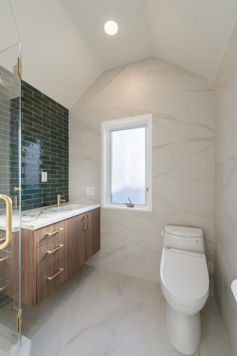 Palo Alto bathroom remodel under a vaulted ceiling, with a green tile accent wall behind the walnut floating vanity, a frosted casement window, a bidet toilet, and large-format marble-look porcelain on walls and floor.