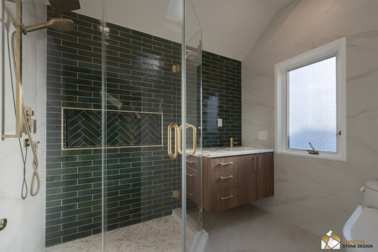 Palo Alto bathroom remodel wide view with the glass shower in deep green subway tile and its herringbone shampoo niche trimmed in brass Schluter profile at left, brass door pulls, and the walnut vanity beneath the frosted window at right.
