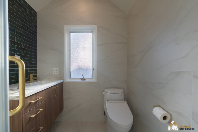 Palo Alto bathroom remodel seen from inside the shower, looking past the brass door handle to the walnut vanity, brass faucet, frosted window, bidet toilet, and brass paper holder on marble-look porcelain.