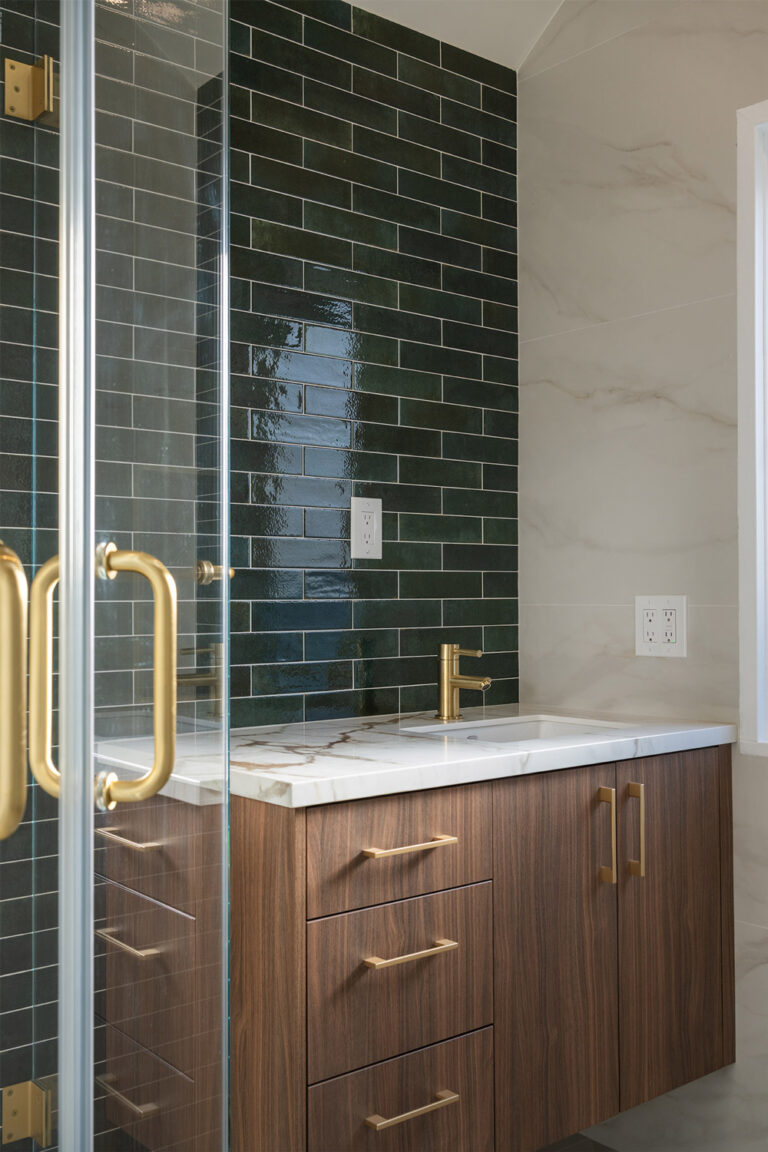 Palo Alto bathroom remodel vanity in close view, its walnut grain and brushed brass pulls set below a Calacatta-look top with amber veins, against the glossy green tile wall and the brass-handled shower door.