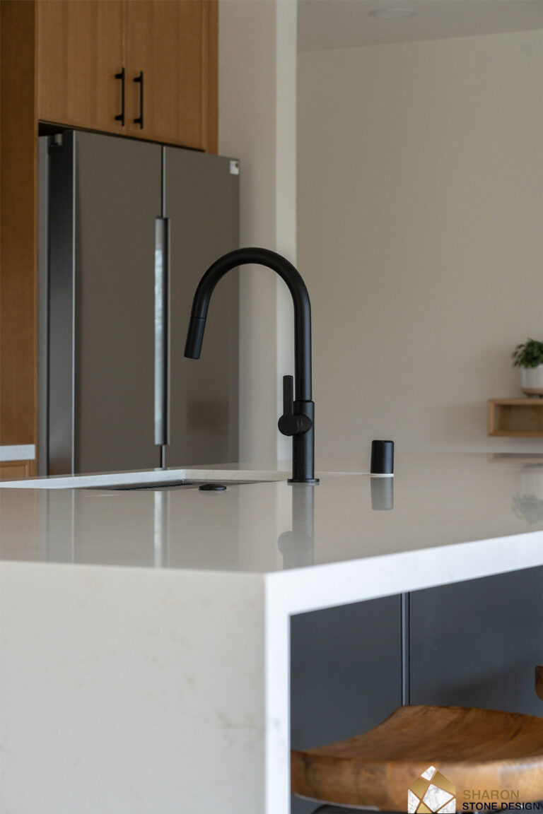 Redwood City home remodel faucet detail from a low angle, the black gooseneck and soap dispenser mirrored in the polished quartz island top, with the stainless refrigerator behind.