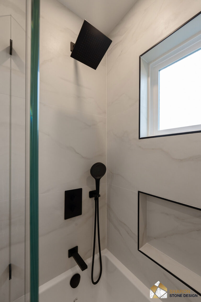 Redwood City home remodel tub and shower detail with a matte black square rain head, handheld shower, thermostatic valve and tub spout mounted on marble-look porcelain beside a window and shampoo niche trimmed in black Schluter profile.