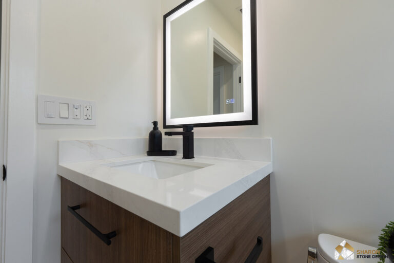 Redwood City home remodel powder room vanity in walnut with a mitered quartz top and upstand, a matte black square-spout faucet and soap dispenser, below a black-framed illuminated mirror.