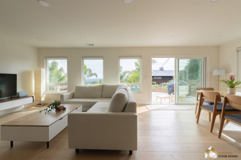 Redwood City home remodel living room with a low white and oak media unit, three windows along the wall, and a sliding door opening to the patio.