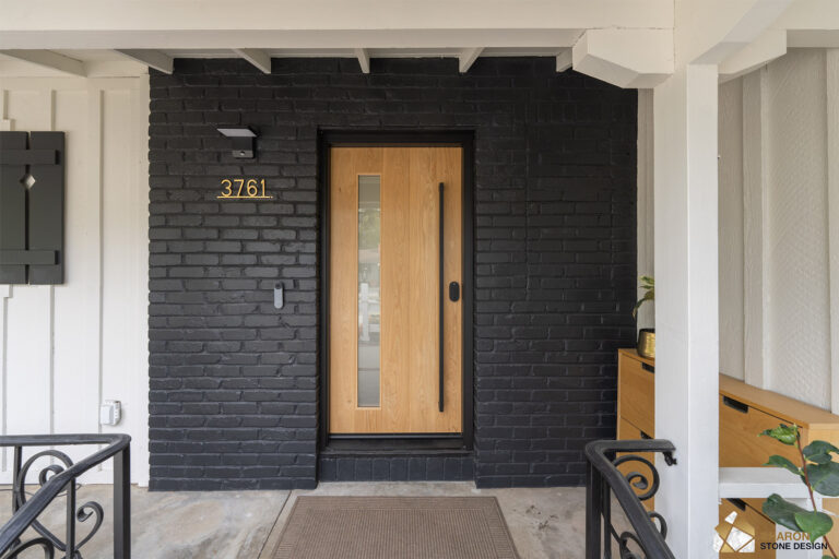 After remodel: the Redwood City entry with the porch brick painted matte black, a white oak door fitted with a full-height black pull and slim vision panel, brass house numbers, and a video doorbell.