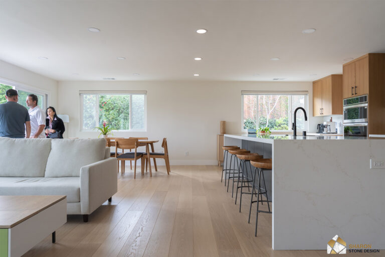 Redwood City home remodel open-plan living space with the quartz island running along the kitchen at right and the two-tone oak and charcoal cabinetry beyond.