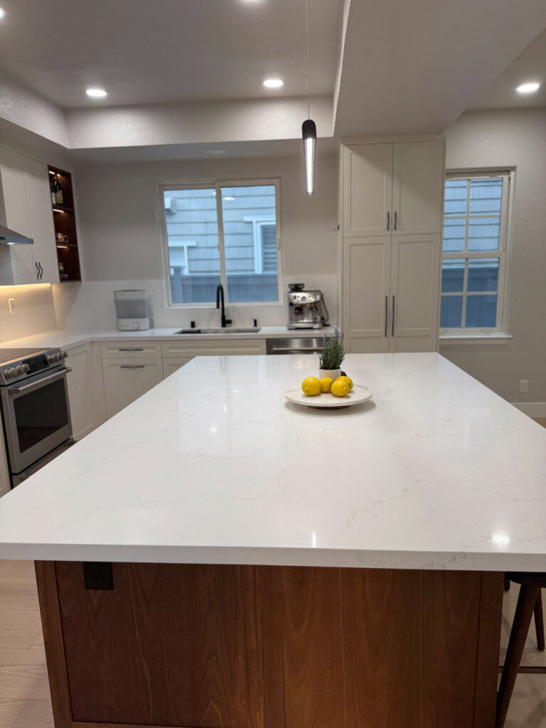 Redwood City home remodel island surface stretching toward the sink run, its white quartz with soft veins running beneath a slim black pendant.