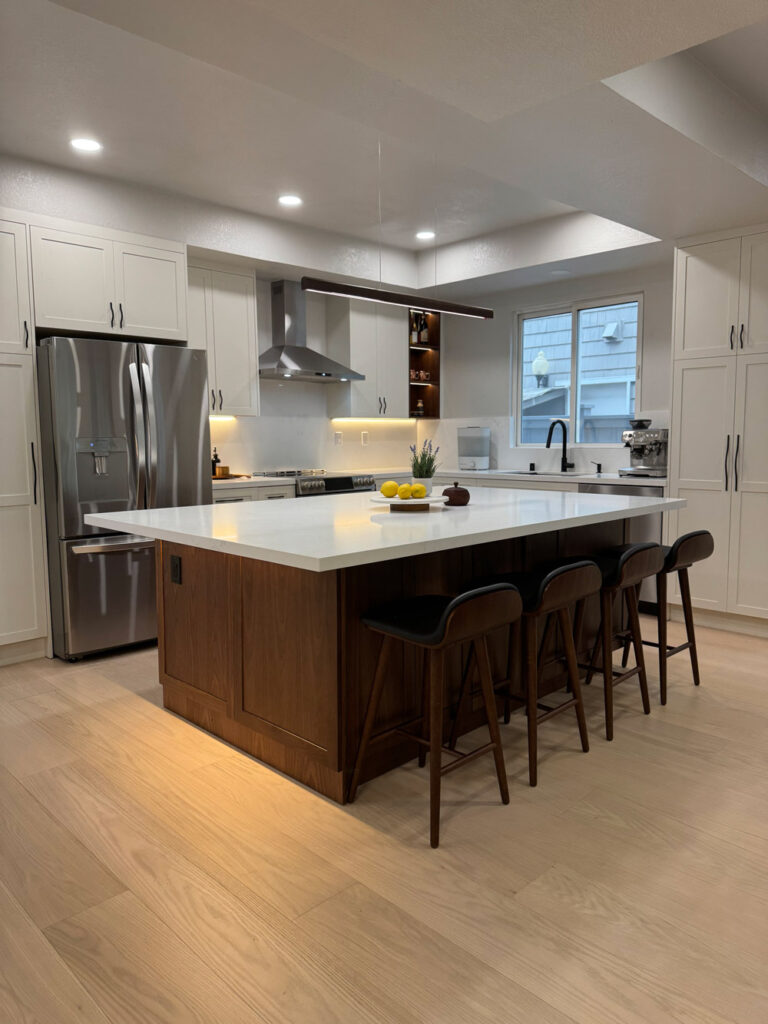 Redwood City home remodel kitchen with white shaker cabinetry wrapping the room, a stainless refrigerator and chimney hood, and an LED-lit walnut bottle niche.