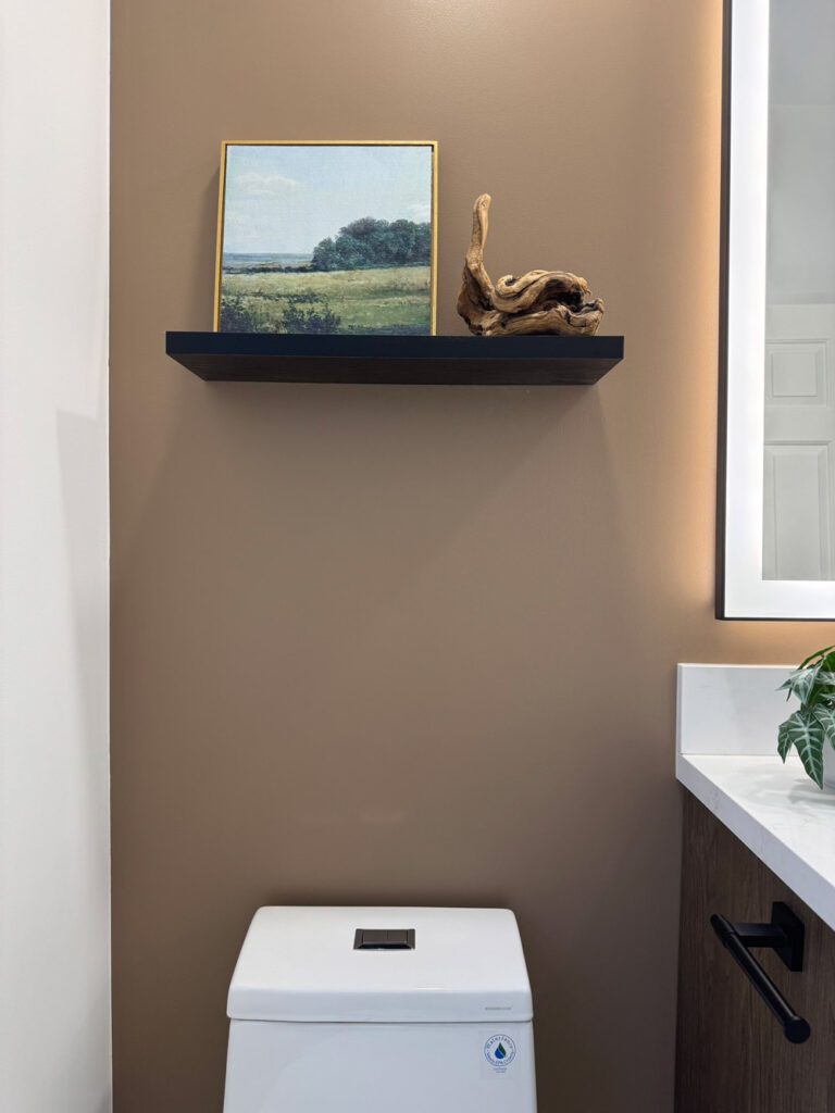 Redwood City home remodel bathroom with the black floating shelf above the toilet, the mocha wall wrapping to meet the illuminated mirror and quartz vanity at right.