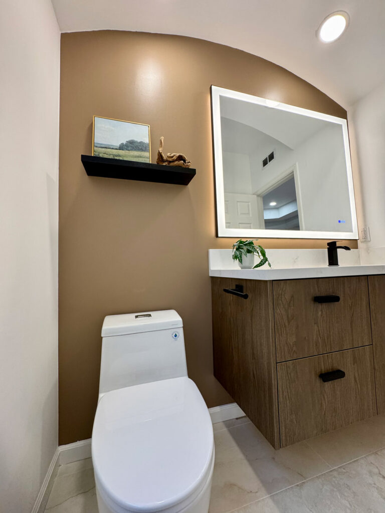 Redwood City home remodel bathroom beneath its curved ceiling, the mocha feature wall holding the black floating shelf beside the backlit mirror and dark oak vanity.