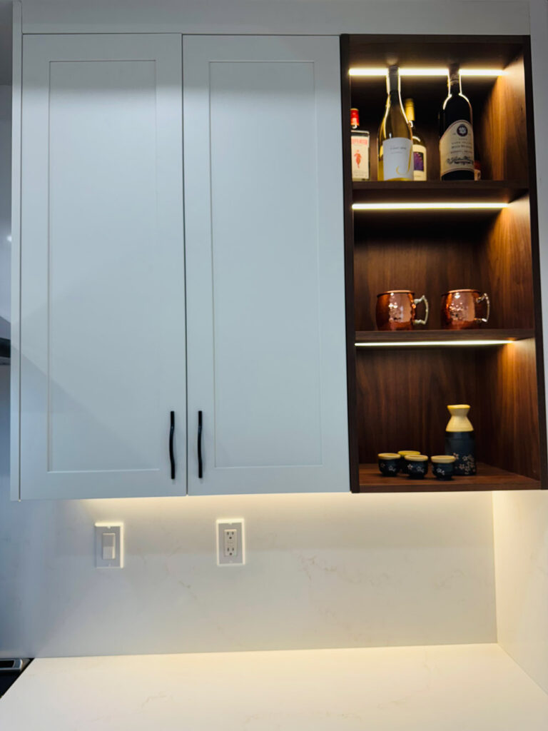 Redwood City home remodel upper cabinetry detail, white shaker doors with black pulls meeting an LED-lit walnut open shelving unit.
