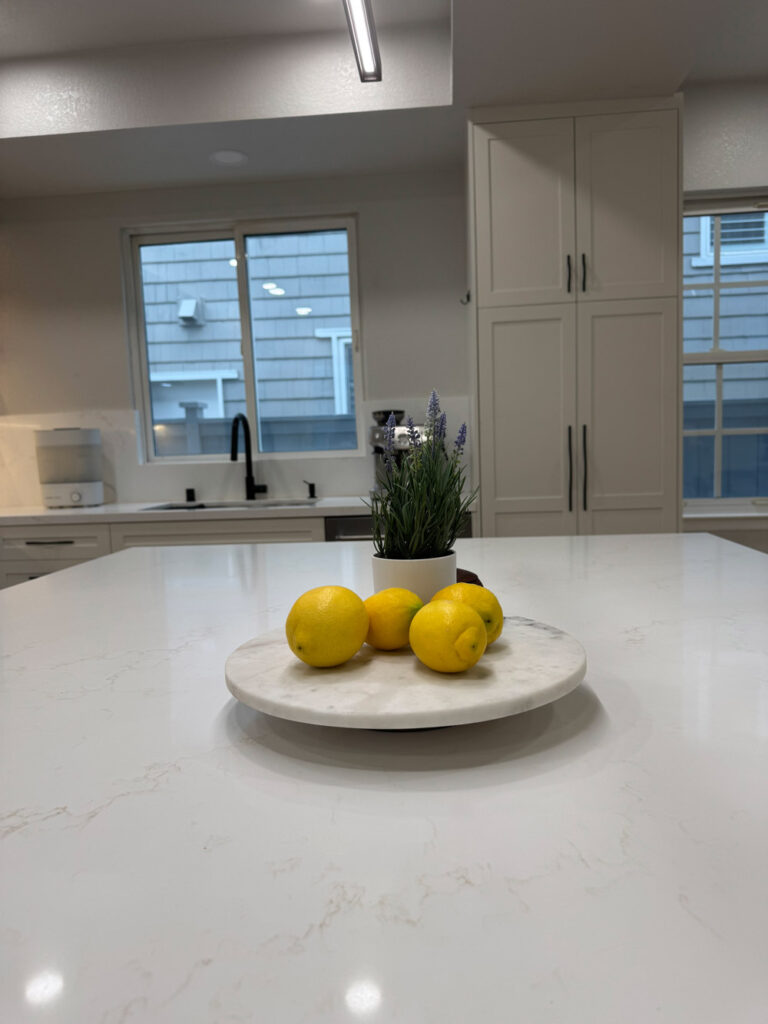 Redwood City home remodel island close-up with the white quartz top in focus, the sink run with its black faucet and the tall white pantry softly out of focus behind.