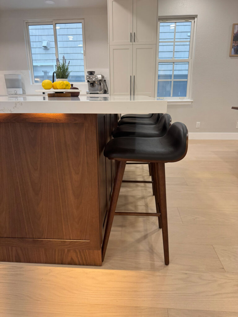Redwood City home remodel island from the seating side, the quartz overhang carried on walnut paneling above pale oak flooring.