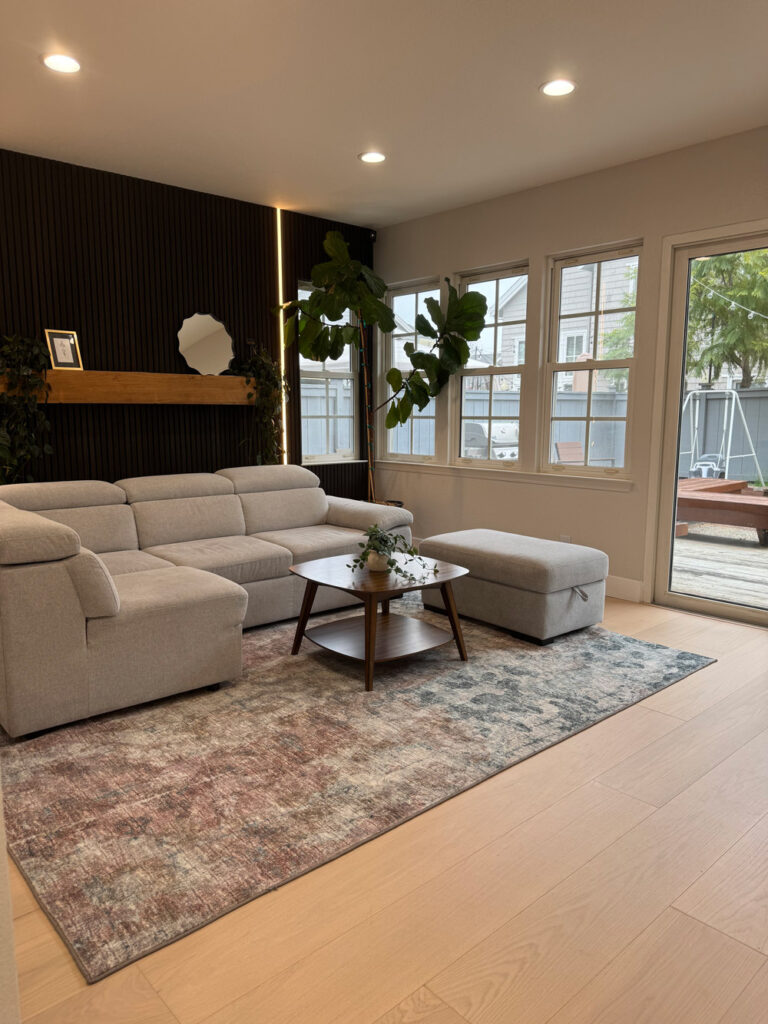 Redwood City home remodel living room corner with the LED-lit black slat wall and oak mantel, and a glazed door opening to the rear deck.