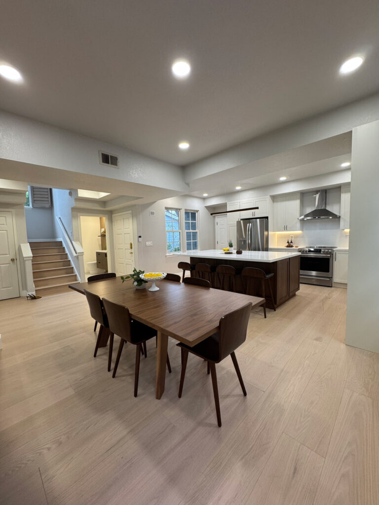 Redwood City home remodel great room with the kitchen island and stainless range at center, and the staircase and entry doors along the left-hand wall.