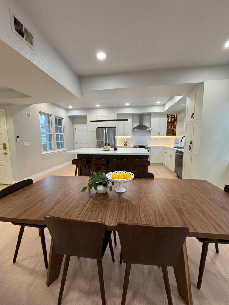 Redwood City home remodel looking straight across to the kitchen, with the quartz island, white shaker cabinetry, and the LED-lit walnut bottle niche at right.