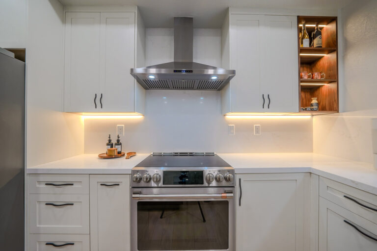 Redwood City home remodel range wall with a stainless chimney hood above a slide-in range, a white quartz slab backsplash, under-cabinet LED strips, and a warm walnut open shelving unit.