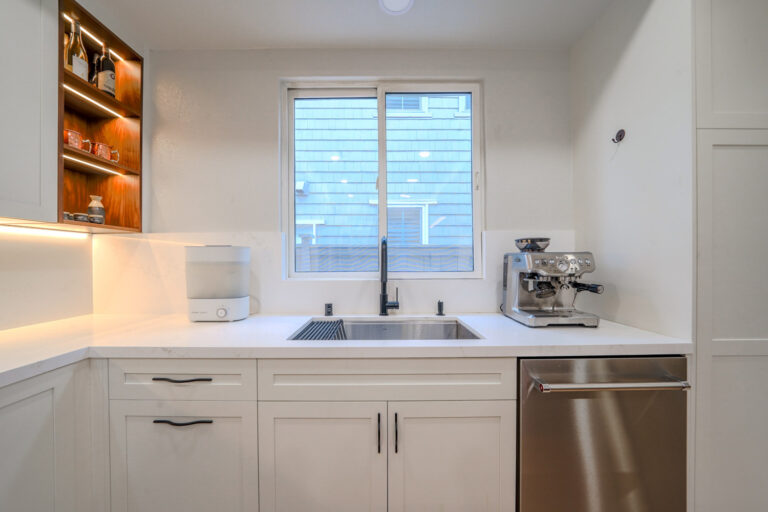 Redwood City home remodel sink run with an undermount stainless sink and matte black faucet below a window, and an integrated stainless dishwasher in the quartz-topped run.