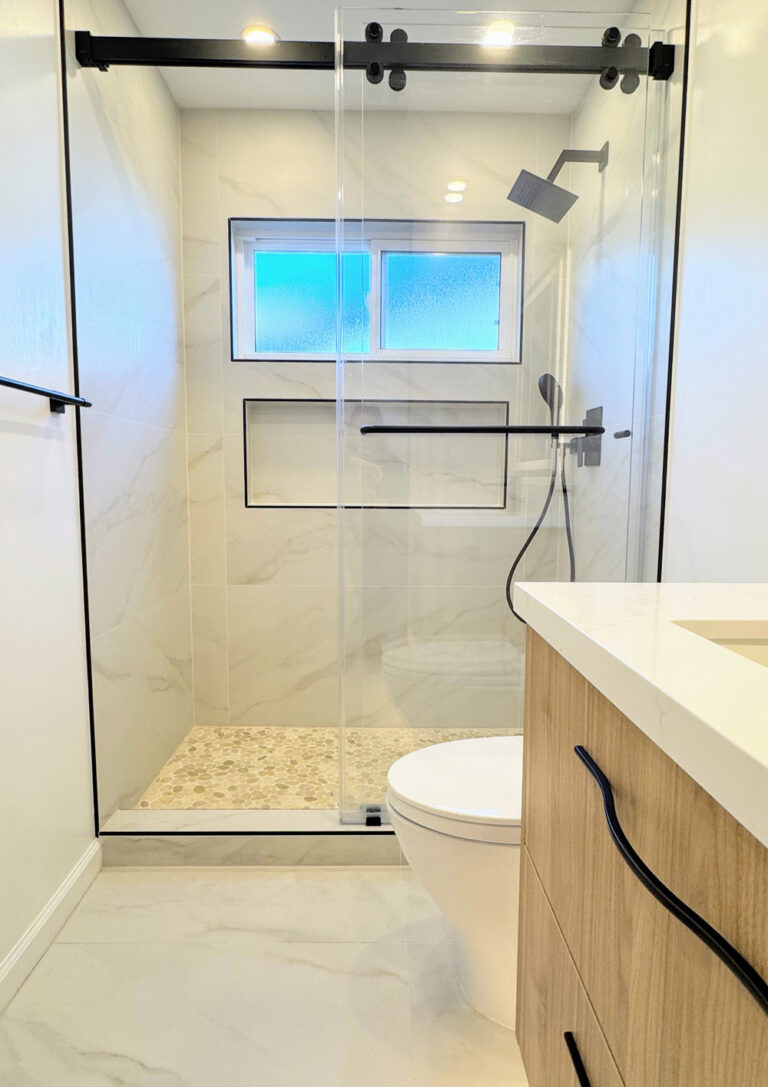 San Jose bathroom remodel showing the shower on its black sliding rail beside the toilet, with the walnut vanity and its quartz top and wavy black pull entering the frame at right.