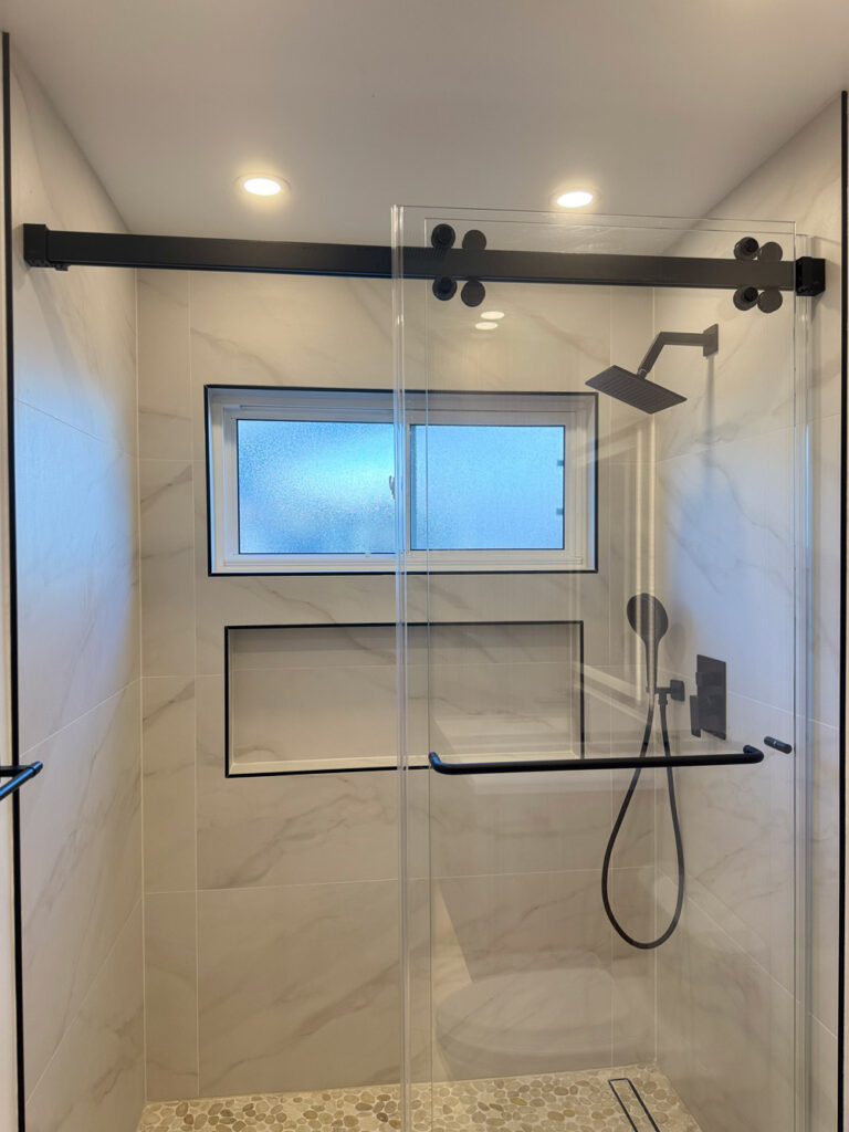 San Jose bathroom remodel shower enclosure with its full black roller rail, an obscured window glowing above the long shampoo niche, and a black towel bar mounted across the glass.
