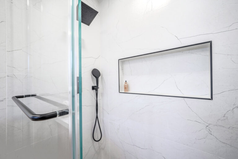 San Jose bathroom remodel shower detail with a matte black square rain head, a round handheld on a black hose, a long shampoo niche trimmed in black Schluter profile, and a black towel bar on the glass panel.