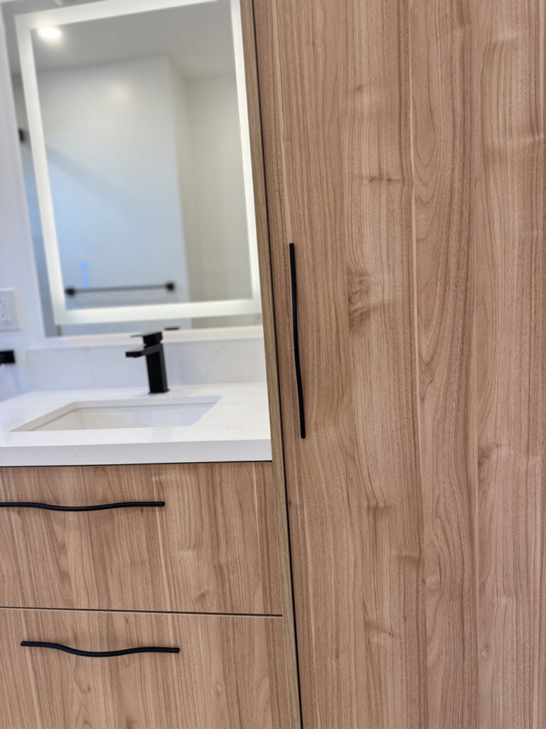 San Jose bathroom remodel joinery detail where the walnut linen tower meets the floating vanity, its long slim black pull set against the vertical grain beside the lit mirror.