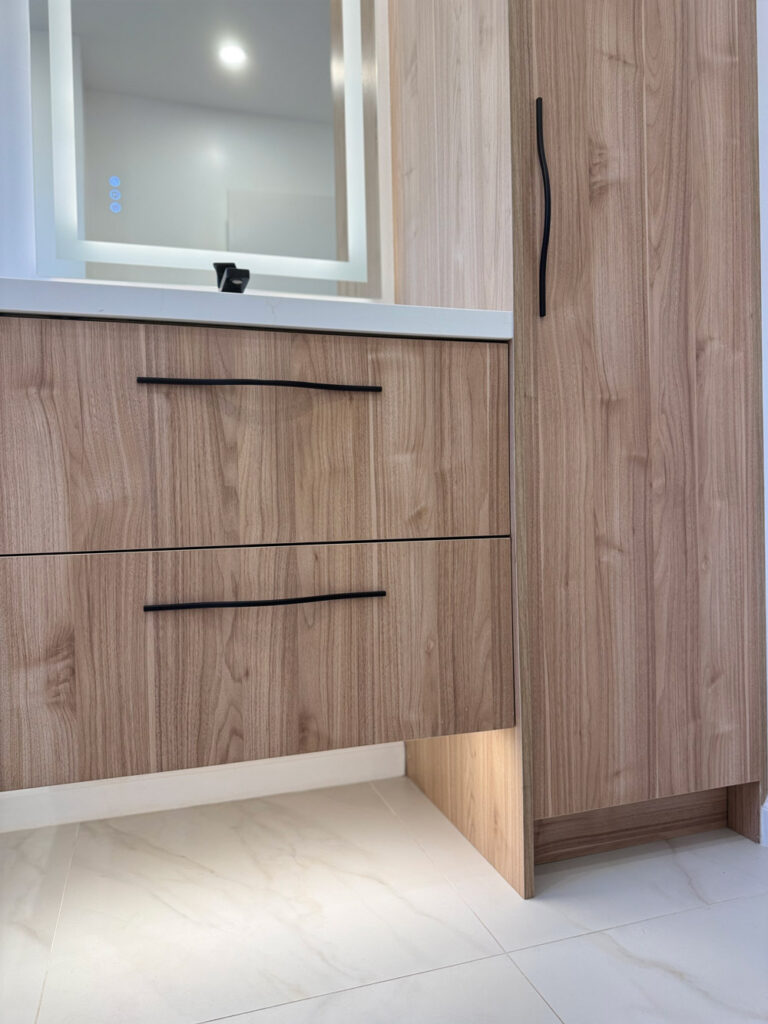 San Jose bathroom remodel joinery from a low angle, the walnut vanity drawers with sculpted black pulls floating above marble-look tile with concealed lighting glowing beneath the linen tower.