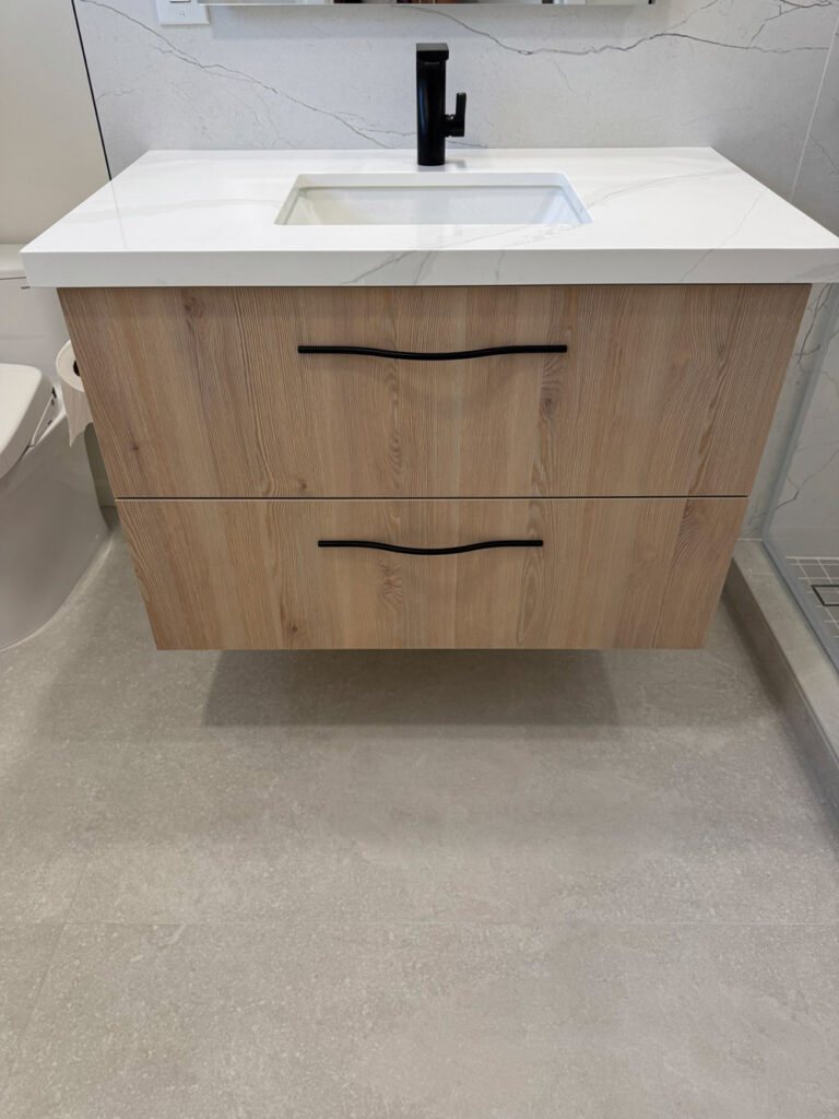 San Jose bathroom remodel vanity photographed head-on, a pale oak floating cabinet with sculpted black pulls beneath a thick quartz top, undermount basin and matte black faucet.