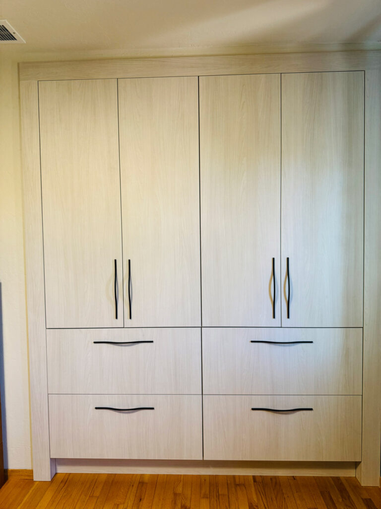 San Jose remodel bedroom wardrobe built in pale whitewashed oak, with four full-height doors above four deep drawers, all fitted with slim sculpted black pulls, set against original hardwood flooring.